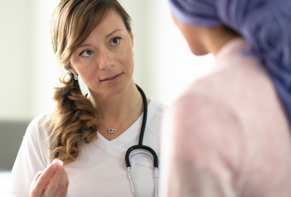 Shot over the shoulder of a young white female doctor facing the camera talks to female patient who has her back to the camera