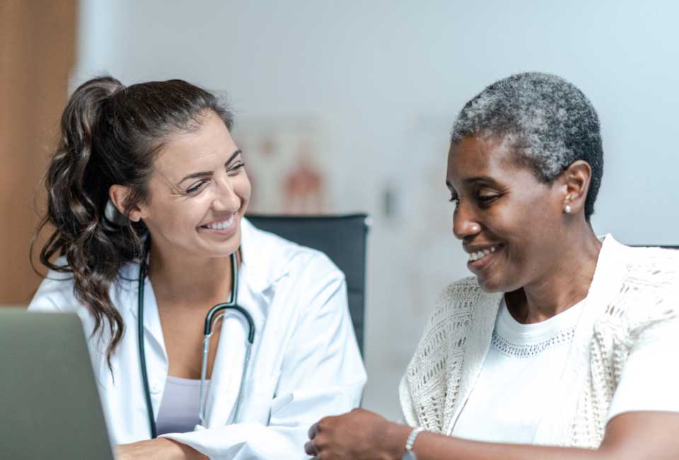 Middle-aged white female nurse sitting with elderly white male patient and showing him information on an iPad